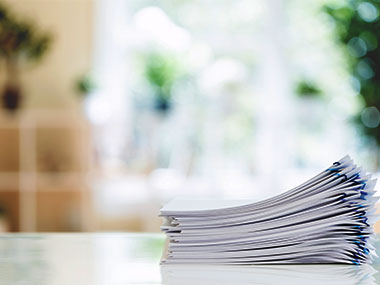 A medium stack of documents on top of each other on a desk.