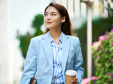 Woman in suit, holding coffee and looking up