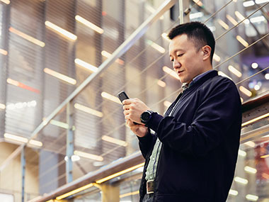 A man stands a lobby area in a tall building while using his phone. 