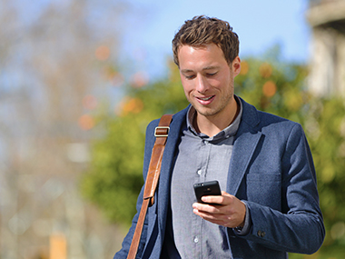 Young businessman walking outdoors, looking at his cell phone.
