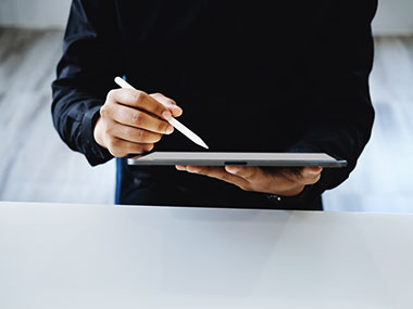 Close up of a man using a tablet and taking notes with a stylus. 