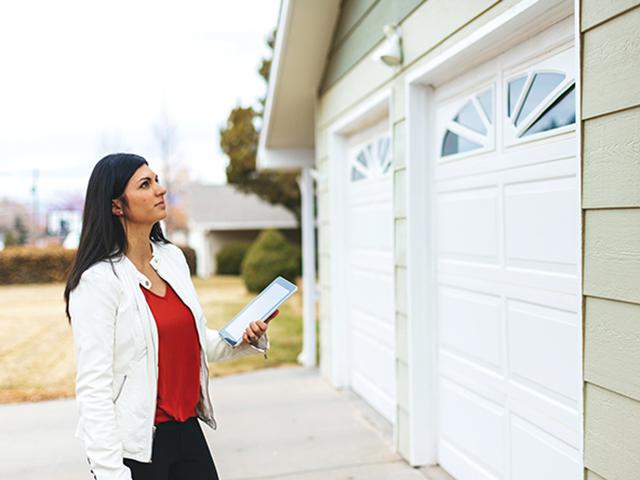 Woman, holding a mobile device, standing looking at a garage door of a house 