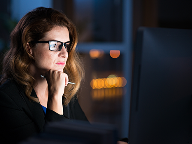 A woman with glasses at night looking at her computer screen