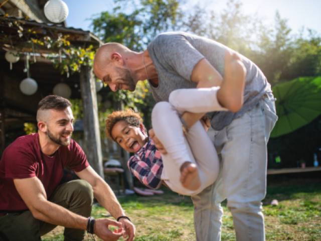 A gay couple play outside with their child