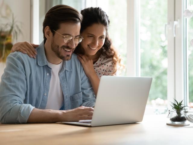 A couple smiling while looking at a laptop