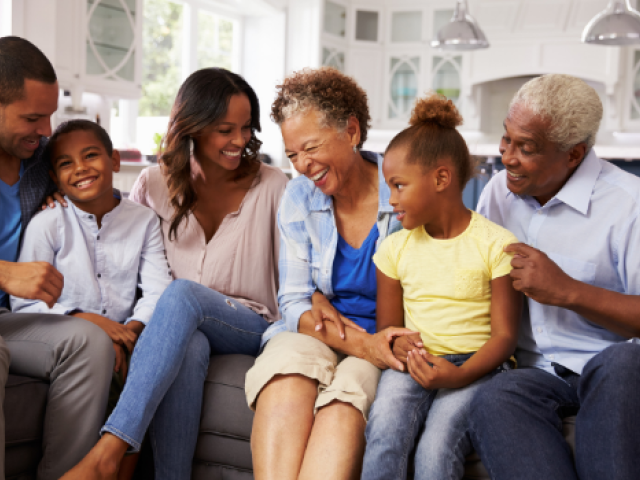 A couple sits on the couch with their children and grandparents while they all smile
