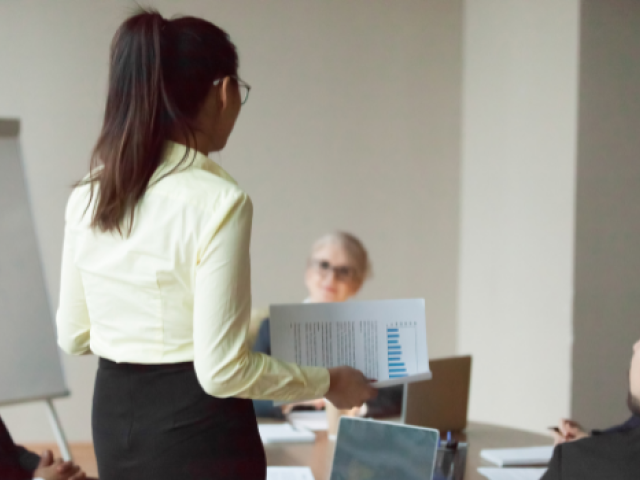 A woman is standing as she presents information to her coworkers in a meeting