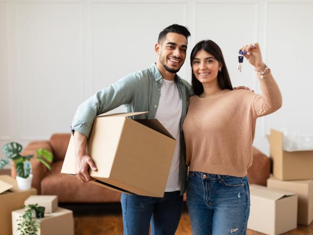 A couple holding the keys to their new home surrounded by boxes.